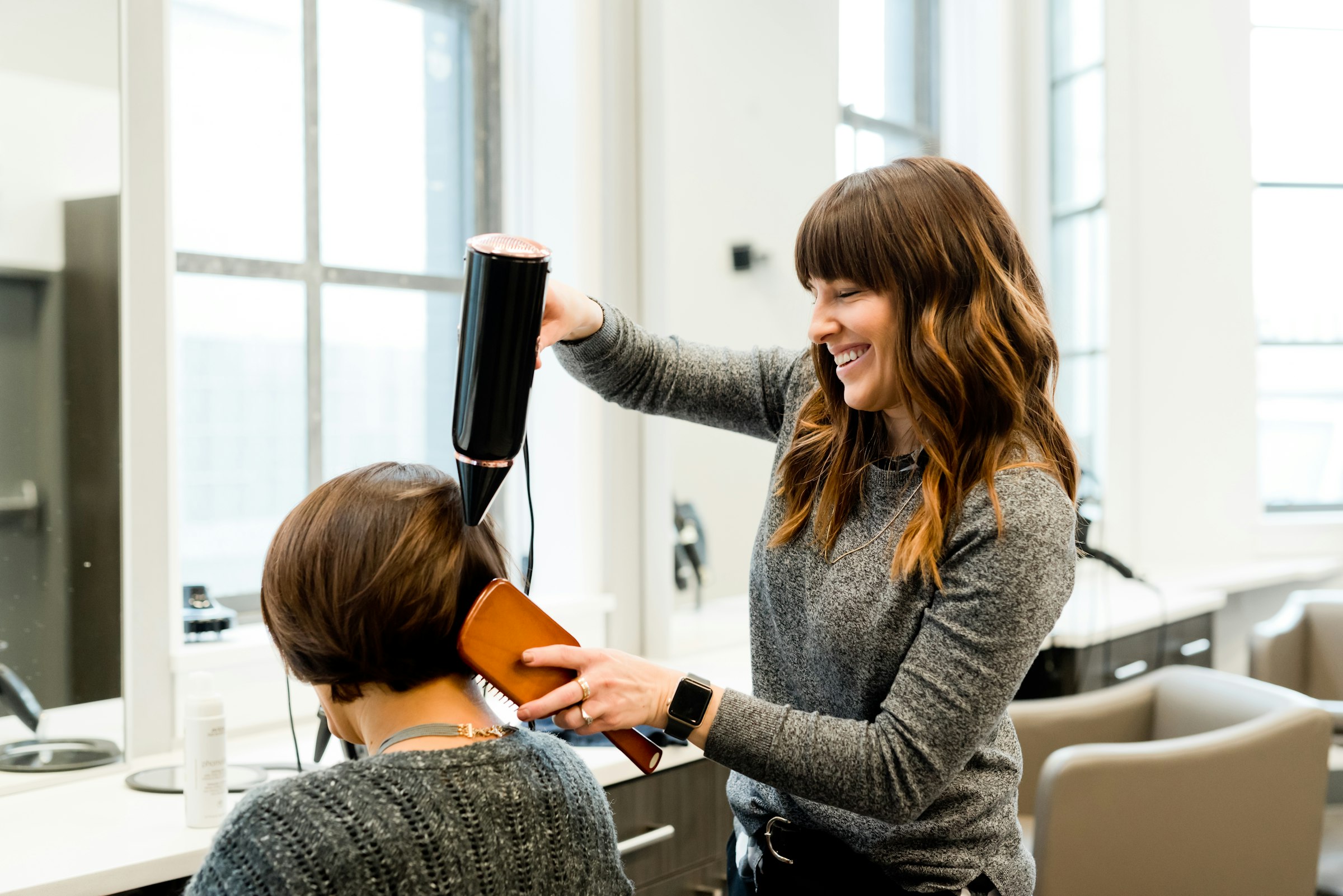 Stylistin föhnt einer Kundin das Haar im hellen Salon